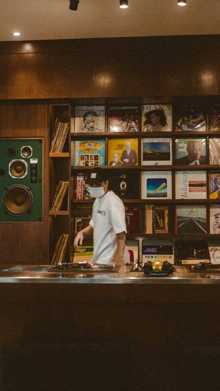 Masked employee organizing vinyl records in a cozy record store, reflecting pandemic norms.